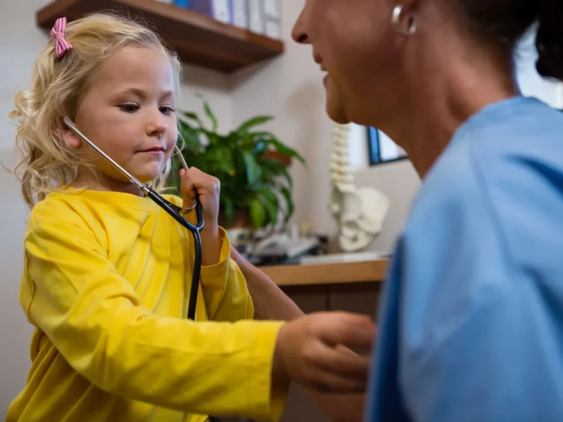 A child listening to a clinician’s chest with a stethoscope
